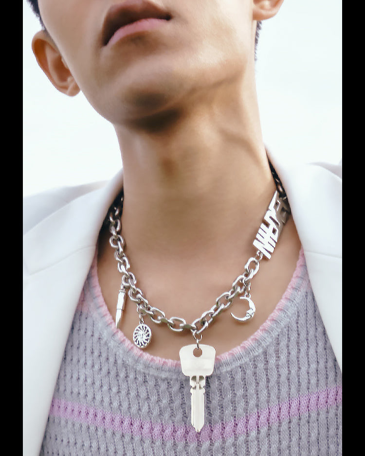 Close-up of a person wearing a silver chain necklace with key pendant on a white background