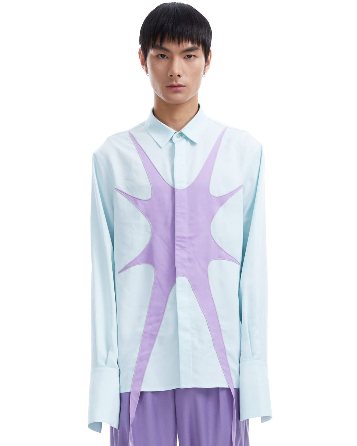 Person wearing a light blue shirt with a star design and purple pants on a white background