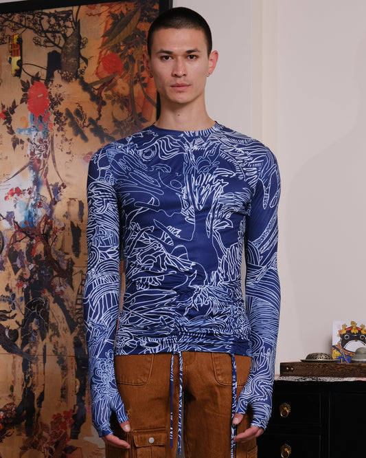 Person wearing a blue patterned shirt and brown pants standing in a room with a decorative wall and furniture.