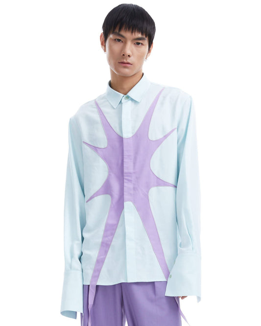 Person wearing a light blue shirt with a purple abstract design and matching pants on a white background