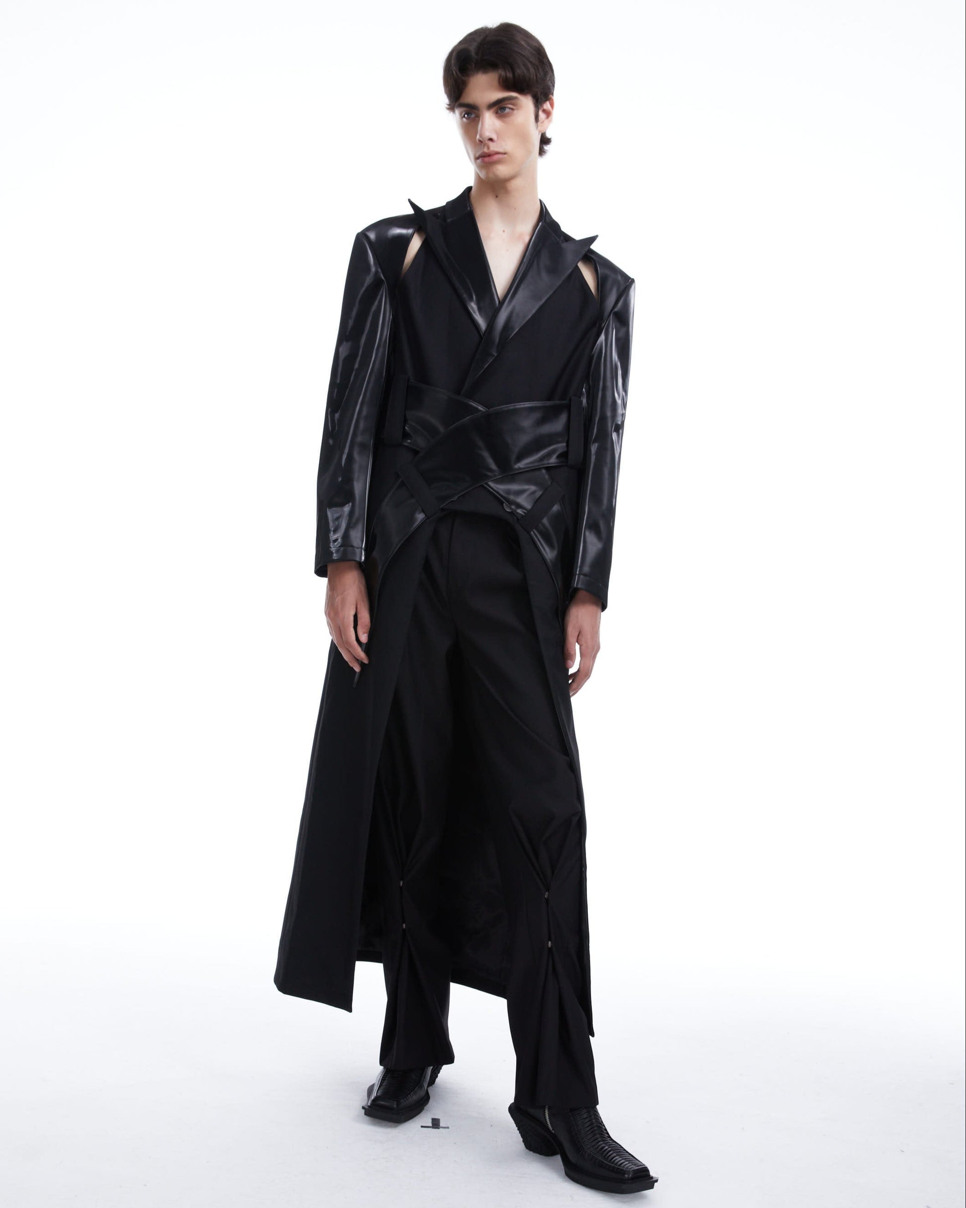 Person wearing a black outfit with a long coat on a white background